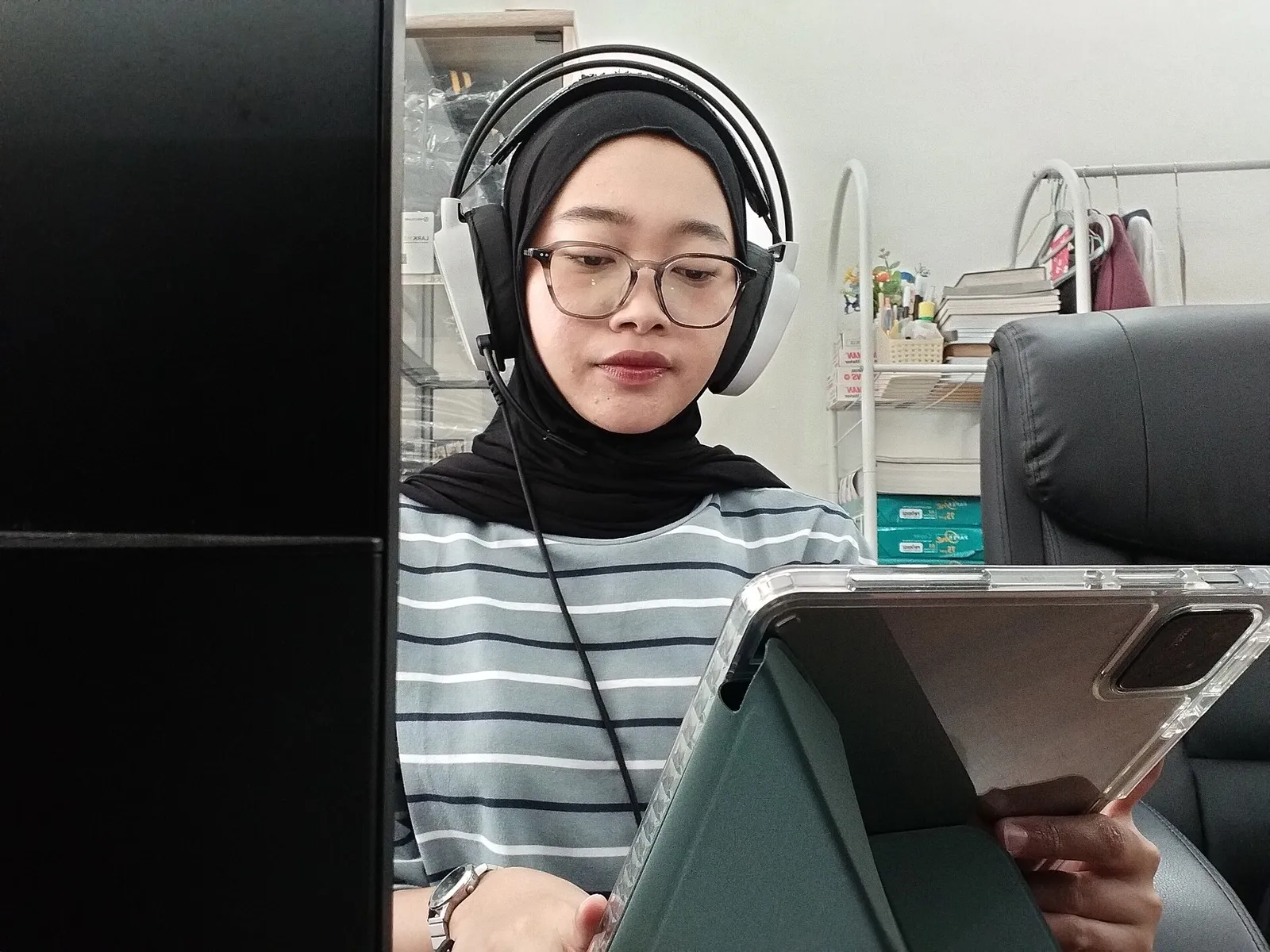 Mahasiswi memakai headphone sambil menyunting di tablet